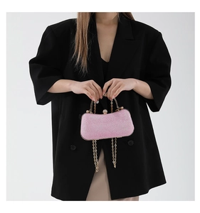 Pink sequin evening clutch bag with gold metal handle held by model in black suit