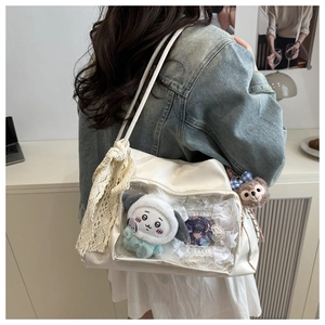 Close-up of white Ita bag with transparent PVC window displaying anime plushies and badges