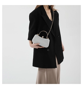 Detail of silver glitter clutch bag with golden top handle and pearl clasp on a suit
