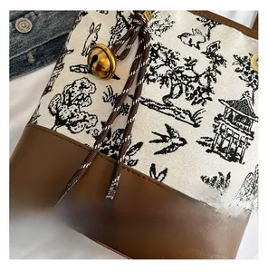 Detailed embroidery of Chinese style rabbit on white canvas bucket bag with brown leather trim