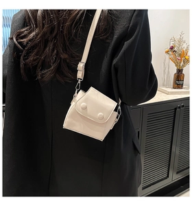 Detail of a chic cream-colored mini crossbody bag styled on a black winter coat