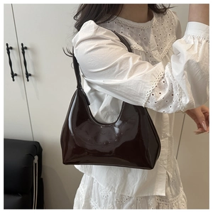 Detail of a shiny dark brown patent leather crescent bag on shoulder with lace top