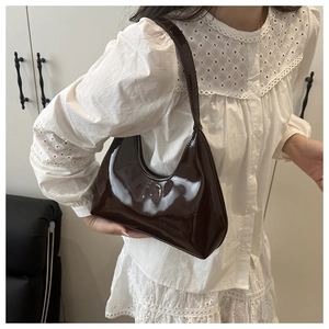 Macro shot of the glossy dark brown patent leather texture on a crescent hobo shoulder bag
