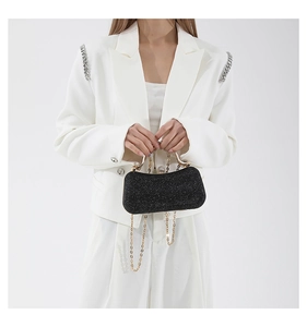 Detail of elegant black sequin evening bag with gold handle and chain on white blazer