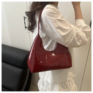 Dark red patent leather crescent hobo bag worn on shoulder by model in a stylish outfit