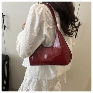 Detail of red patent leather hobo bag with glossy finish and logo carried by model