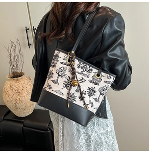 Detail of embroidered landscape bucket bag with black leather base and woven pendant