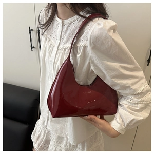 Detail of dark red patent leather crescent bag worn by a model in a white lace shirt