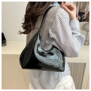 Detail of a black patent leather crescent shoulder bag with silver metal Baggy Cult logo