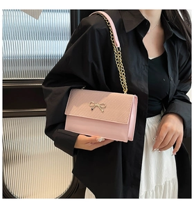 Close-up of pink crossbody bag with gold bow clasp and metal chain on model