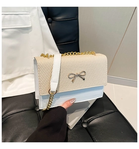 Dettaglio della trama tessuta beige e fibbia a fiocco dorato su borsa a tracolla bianca