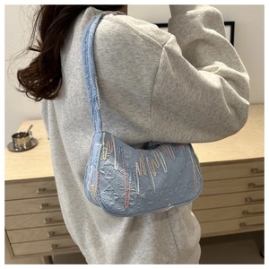 Close-up of light blue hobo bag with colorful wave embroidery worn on model's shoulder