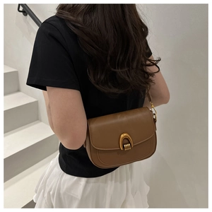 Gros plan d'un sac besace marron avec boucle dorée porté par un mannequin sur escalier