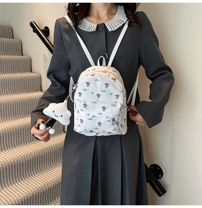 Gros plan d'un mini sac à dos blanc à fleurs avec un charme de nuage et une poche zippée