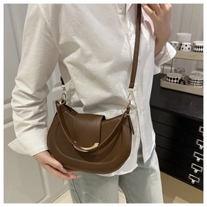 Detail of a brown leather saddle bag with gold crescent buckle worn with casual attire