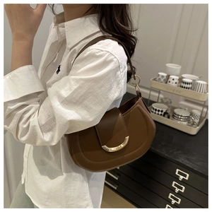 Detailed side view of a brown leather crescent shoulder bag with a gold metal clasp