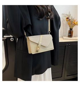 Detail of glitter patchwork and gold rotating buckle on beige leather crossbody bag