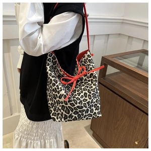 Detail view of leopard print tote bag with red shoulder straps and front ribbon bow accent