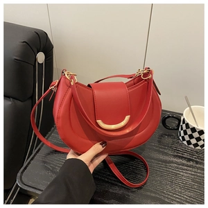 Detail of red crescent saddle bag featuring a prominent gold metal buckle and leather strap