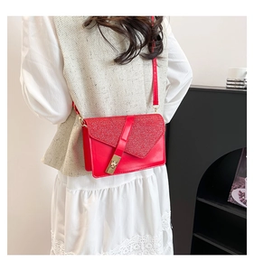Detail of red crossbody bag featuring glitter asymmetric flap and gold twist lock