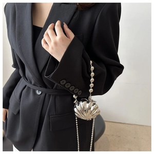 Detail of silver shell-shaped mini bag with pearl bead handle and metallic chain strap