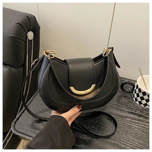 Detail of matte black saddle bag with gold metallic buckle on a minimalist background