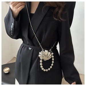 Detail of silver shell-shaped mini crossbody bag with pearl strap on black blazer
