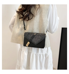 Detail of a black crossbody bag with glitter V-flap and gold buckle shown on a model