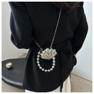 Model wearing a silver shell-shaped mini bag with metallic texture and beaded chain