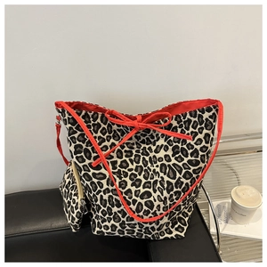 Detail of leopard print tote bag with red bow and matching small pouch on a black bench