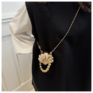 Detail of a golden shell-shaped mini bag with metallic texture and beaded chain straps