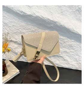Detail of a chic beige crossbody bag featuring a sparkling sequined flap and gold metal clasp