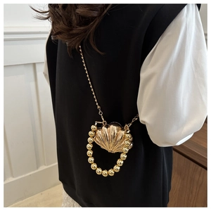 Detail of a golden seashell-shaped mini bag with pearly gold handle and metallic chain