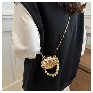 Detail of a golden shell-shaped mini crossbody bag with pearl chain and metallic finish
