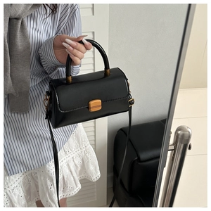 Detail of matte black leather handbag with gold buckle and semi-circular handle in use