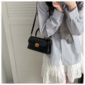 Detail of minimalist black leather bag with gold buckle on a blue striped shirt
