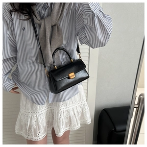 Close-up of black glossy leather handbag with gold lock and sturdy top handle detail