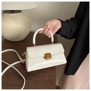 Side view of white leather handbag with gold twist lock and rigid handle in lifestyle setting