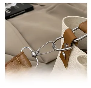 Detail view of the silver metal swivel hook and brown leather strap on a white bucket bag