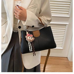 Detail of black pebbled leather bucket bag with brown accents and cute plush charm charm