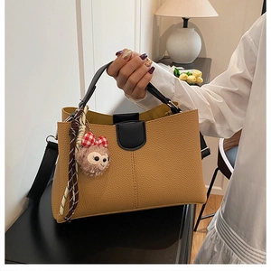 Detail of camel pebbled leather tote with black contrast handles and plush pendant charm