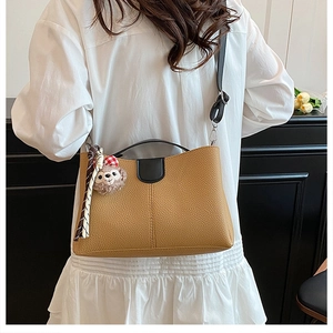 Detail of camel lychee leather bucket bag with wide strap and teddy bear charm