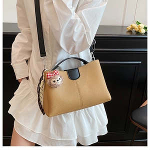 Detail of khaki leather bucket bag featuring a plush charm and decorative silk scarf