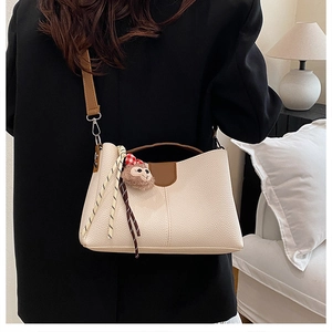Detail of cream white pebbled leather tote with brown handles and a cute plush charm