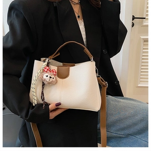 Detail of white lychee textured bag with brown leather handles and plush bear charm