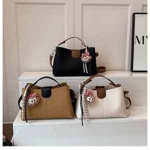 Close-up of three tote bags in black, tan and cream with plush bear charms on display
