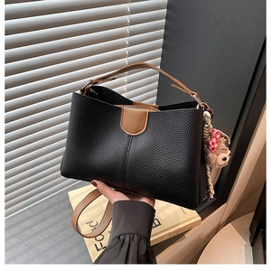 Detail of black lychee grain leather tote bag with brown handles and plush bear charm