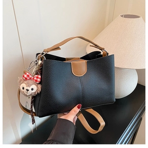 Detail of black lychee grain bucket bag featuring brown handles and a plush doll charm