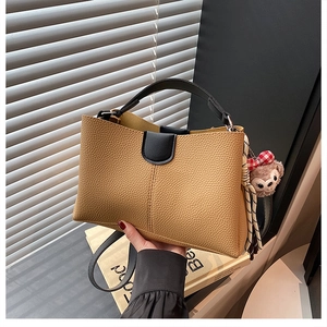 Detailed view of brown lychee-patterned tote bag with black handles and plush bear charm