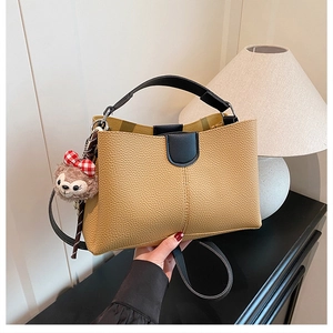 Close-up of yellow pebbled leather tote with black handles and a plush bear charm